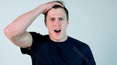 Surprised young man in casual Clothing keeping mouth open and staring at camera while standing against white background