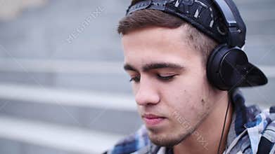 Young trendy man listen to music on smartphone sitting on the steps outdoor