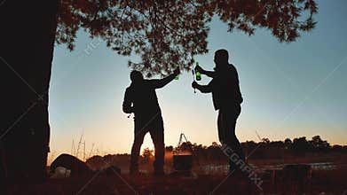 Two men dancing at a camping party on nature fun funny silhouette of sunlight. two tourists on a barbecue have a rest