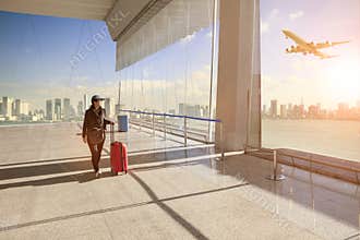 traveling woman with belonging luggage walking in airport terminal building and passenger plane flying over building in city
