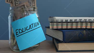 Hand putting dollar bills in jar with label education.
