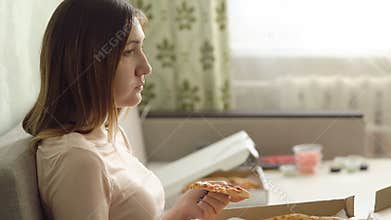 Lonely sad girl with pizza sitting on sofa at home and watches a movie