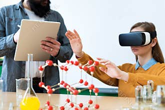 Young teacher using Virtual Reality Glasses and 3D presentation to teach students in chemistry class. Education, VR, Tutoring.