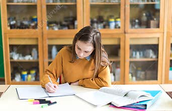Young female college student in chemistry class, writing notes. Focused student in classroom.