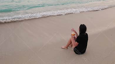A girl drinks a cocktail on a sandy beach