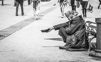 Hungry homeless beggar woman beg for money on the urban street in the city from people walking by, social documentary concept blac