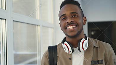 Portrait of young handsome student of african-american ethnicity standing in wide white spacious corridor of college