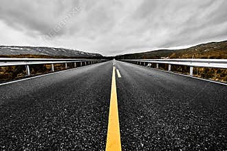 Image of a wide open prairie and mountains with a paved highway road stretching out as far as the eye can see with beautiful natur