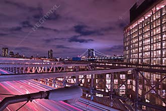 Brooklyn Bridge at Twilight with purple violet hue timing and a well lit building on the right and heavy traffic below