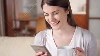 Smiling businesswoman working on mobile phone at home drinking coffee. Home-office concept