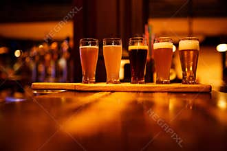 Various types of craft beer in small glasses on a wooden table in a pub.