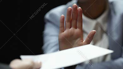 Woman showing stop gesture while man offering white envelope, bribe reject