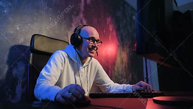 Young pro gamer playing in online video game, talks with team players through microphone. Neon colored room. e-sport