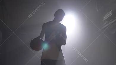 One basketball player playing with ball in misty dark room with floodlight