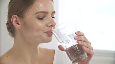 Woman drinking water from glass and looking at camera