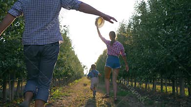 Cheerful family of gardeners playing with kid in orchard during harvesting in backlight