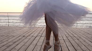 Close up footage of young ballerina`s legs in dance motion. Ballet dancer in long white tutu and pointe exercising