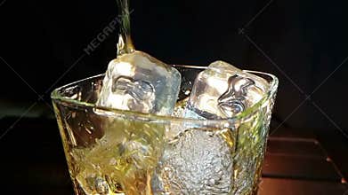 Barman pouring whiskey in the glass with ice cubes on wood table and black dark background, focus on ice cubes, whisky relax time