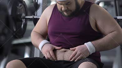Unconfident overweight male in gym looking at his fat belly, weight loss dieting