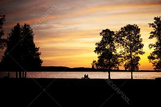 Elderly couple sitting on a bench by lake at sunse