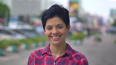 Charming brunette woman smiling at camera and standing on street in urban city, happy and cheerful