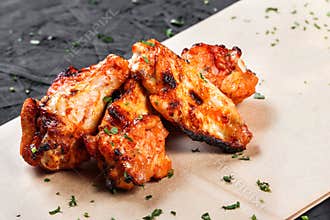 Fried chicken wings with greens on craft paper on black background.