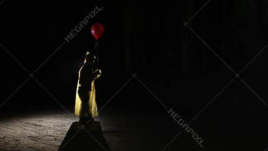 Male silhouette in yellow cloak with red balloon in his hand in dark