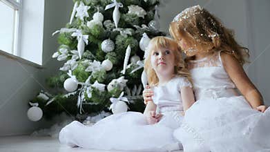 Christmas sisters embrace with artificial snow on hair on background Xmas tree with ornaments