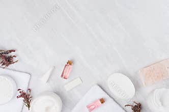 Natural spa white and pink cosmetics products and bath accessories with pink flowers as frame on white wood board, top view.