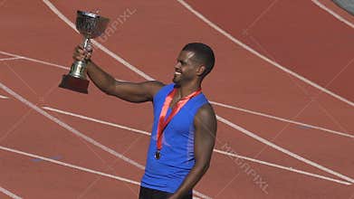 Hispanic sportsman with gold medal on chest holding cup, realizing his victory