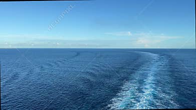 A cruise ship wake in the Atlantic Ocean on a sunny day with dark blue water and clear skies