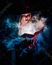 Beautiful witch reading magic book on dark background in forest. Halloween, blonde wizard costume concept. Pretty woman