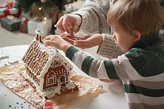 Little boy with mom decorating christmas gingerbread house together, family activities and traditions on Christmas and