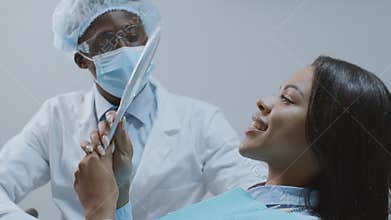 Professional man dentist giving mirror to black female patient, grateful woman enjoying result of treatment at clinic
