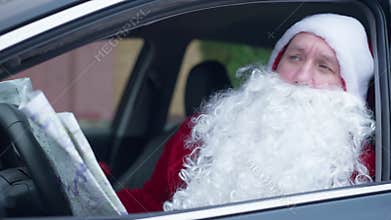 Confused bearded Santa Clause sitting in car on driver&#x27;s seat examining paper map. Portrait of lost Father Christmas in