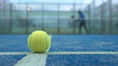Yellow ball on floor behind padel net in court outdoors. Man playing paddle.