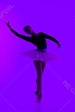 Beautiful ballerina on purple background dancing ballet. Woman performs smooth movements. Sensual dancer in tutu dress