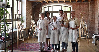 Group of diverse people holding paintbrushes, posing in art studio