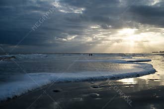 Sunset with Light Beams over the Ocean with Foamy Waves on the Beach