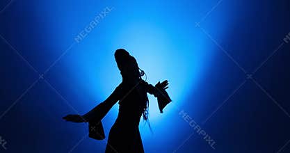 Silhouette of woman with long hair dancing in blue light and smoke