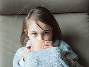 A girl drinks cocoa in a chair.