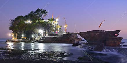 Pura Tanah Lot, home to ancient Hindu pilgrimage temple on natural rock formation with light, trees & pilgrims, at Bali, Indonesia