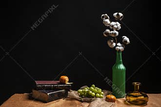 Still life with cotton branches in green bottle, bunch of grapes