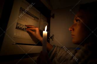 Woman in total darkness investigating fuse box at home during power outage or blackout. No electricity concept