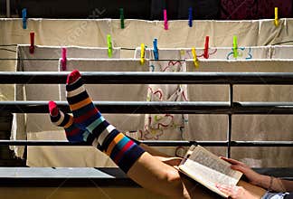 A girl in colorful striped socks is reading a book on the balcony in front of some clothes hanging out to dry Italy, Europe
