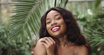 Beautiful girl with tanned skin African American with a bare top, being among tropical plants. Natural makeup and wet
