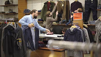 Wide shot of Caucasian men and women fighting for clothes in shop during black friday sales. Male and female clients