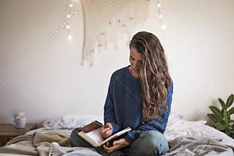 Woman sat on bed writing in her journal
