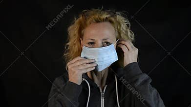 Middle-aged blonde woman demonstrates how to use the face mask to protect herself from the risk of contagion from covid-19