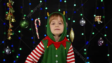 Kid girl in Christmas elf Santa helper costume dancing, fooling around. New Year holiday celebration